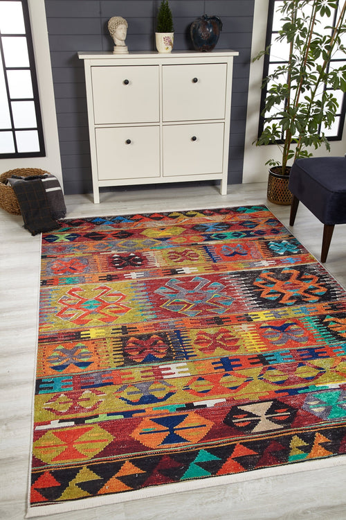 Load image 1 in gallery view. The Serene Sahara - Washable Rug - JR1959, with its vibrant geometric patterns, brightens the light wood floor. Perfect for high-traffic areas, it sits by a white cabinet with decor, a potted plant, and a dark cushion in an airy, sunlit room.