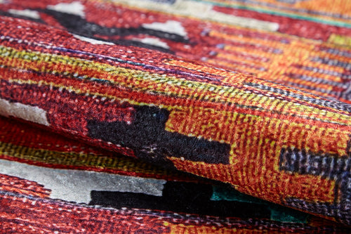 Load image 1 in gallery view. Close-up of the Serene Sahara - Washable Rug - JR1959, featuring bold red, orange, yellow, black, and white geometric patterns. Its folded fabric highlights texture—ideal for high-traffic areas and easy washing.