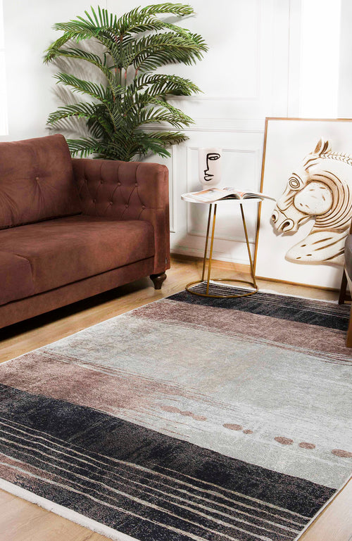 Load image 1 in gallery view. A modern living room with a brown sofa, green potted plant, small round side table holding a cup and magazine, horse painting on the floor, and the Serene Swirls - Washable Rug - JR952—ideal for high-traffic areas.