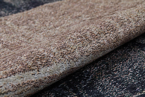 Load image 1 in gallery view. A close-up of the Serene Swirls - Washable Rug - JR952, featuring a speckled bronze and brown pattern, rolled up on a darker, matching surface—ideal for high-traffic areas.