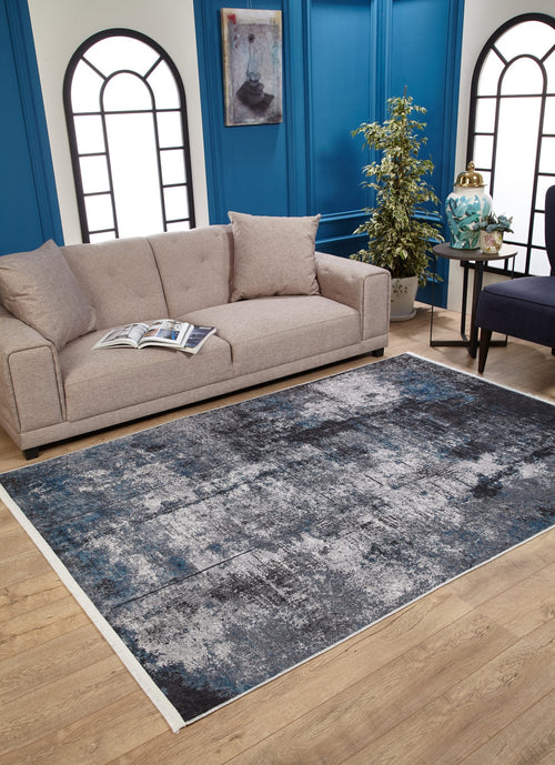 Load image 1 in gallery view. A beige sofa with cushions and an open book sits on a wooden floor beside the Solar Eclipse - Washable Rug - JR1921. Blue paneled walls, large windows, and modern decor create a bright, stylish living room ideal for high-traffic areas.