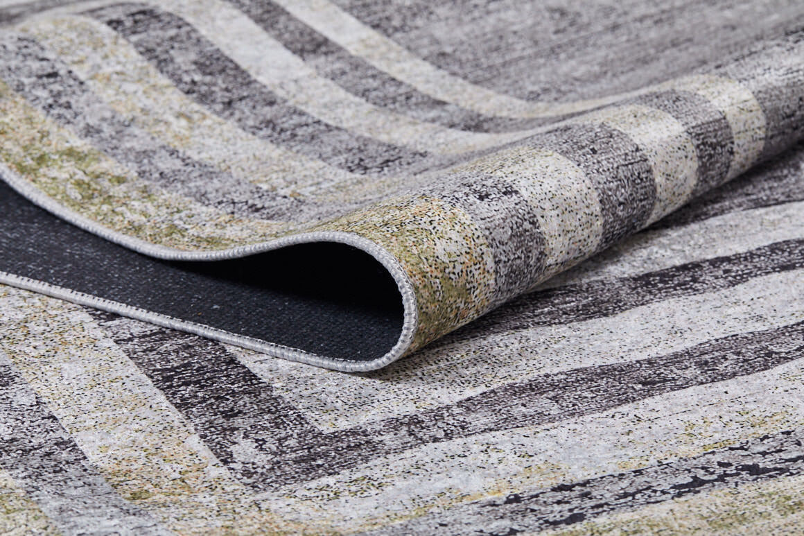 A close-up of the Sophisticated Trellis - Washable Rug (JR1194) shows its folded corner, revealing grey, black, white, and light yellow stripes and speckles—ideal for high-traffic areas. The edge and underside are also visible.