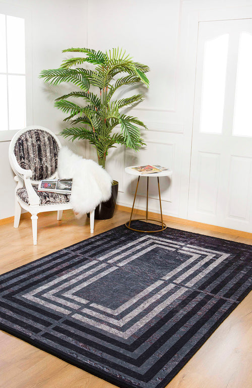 Load image 1 in gallery view. A modern living room showcases the Sophisticated and Chic - Washable Rug - JR1409, a geometric black flat-weave rug, paired with a white ornate chair, black-and-white cushion, fur throw, round side table, potted plant, and wood floors.