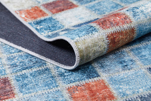 Load image 1 in gallery view. Close-up of the Square Serenity - Washable Rug - JR1255, featuring a blue, red, and cream checkered pattern. The slightly folded rug reveals its textured material and stitched edging—perfect for high-traffic areas.