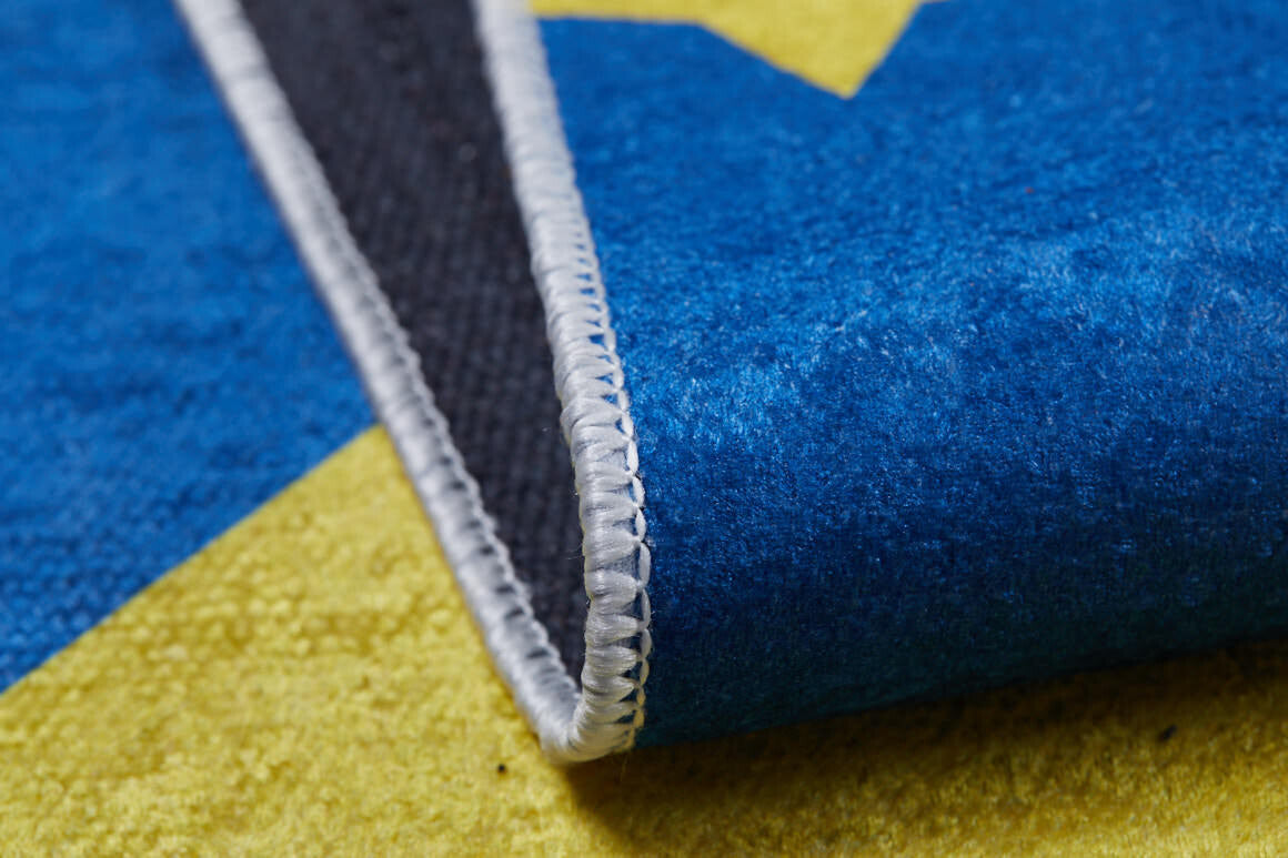 A close-up of the Starry Dreams - Machine-Washable Rug JRC004, featuring a vibrant blue, yellow, and black pattern with detailed edge stitching, highlights its allergy-sensitive material as the rug is slightly folded.
