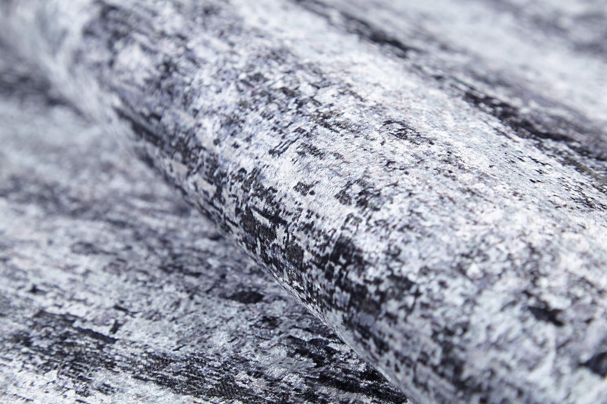 A close-up of a roll of textured wallpaper in mottled gray, black, and white—resembling stone or brushstrokes—pairs perfectly with the Stone Path - Washable Rug - JR1772 for a coordinated look in high-traffic areas.