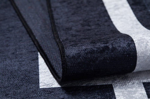 Load image 1 in gallery view. Close-up of the Subtle Border - Washable Rug - JR597 in black with a white geometric pattern; its edge is lifted, showing the soft, thick, and washable surface—ideal for high-traffic spaces.