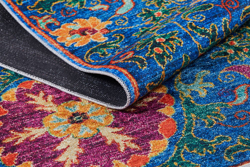 Load image 1 in gallery view. A close-up of the Summer Bouquet - Washable Rug - JR1358 showcases vibrant blue, red, yellow, and orange floral patterns. A folded corner reveals its detailed washable texture—ideal for high-traffic areas.