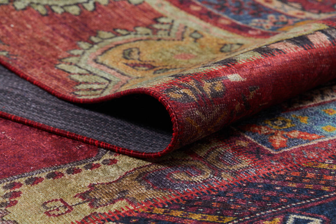 A close-up of the Tapestry Tango - Washable Rug - JR313 showcases its vibrant red, beige, and gold patterns. This rug is partially folded to reveal a textured underside—perfect for high-traffic areas and easy cleaning.