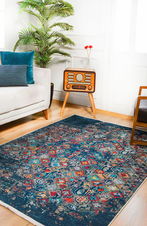 Bild 1 in Galerieansicht laden. A living room features a white sofa, blue cushions, a vintage radio on a wooden stand, a potted plant, and the Tarnished Elegance - Washable Rug - JR1095—perfect for high-traffic areas—on a wooden floor with sunlight streaming in.