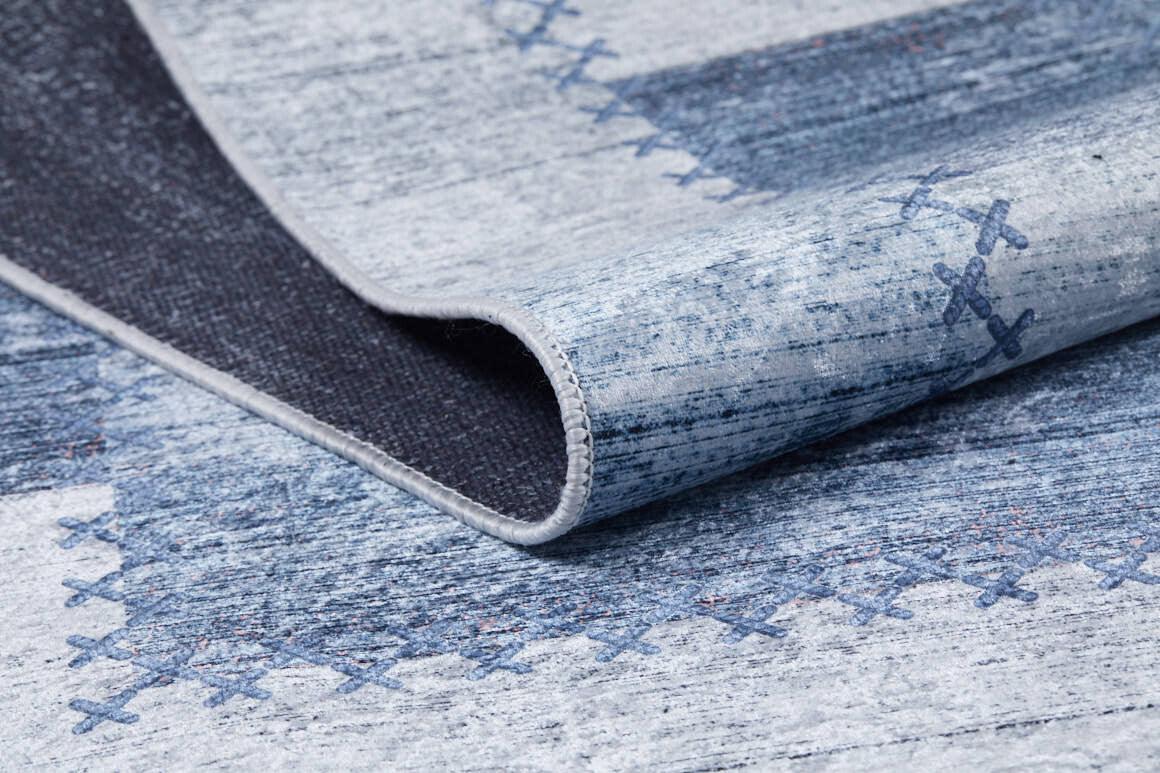 A close-up of the Tartan Twist - Washable Rug - JR31, featuring a folded blue and gray corner with faded patterns and dark blue crisscross stitching—perfect for homes with allergy sensitivities.