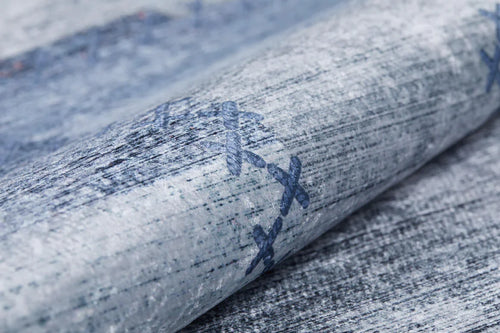 Load image 1 in gallery view. Close-up of Tartan Twist - Washable Rug - JR31: rolled light blue denim fabric with visible texture and dark blue X-shaped embroidery, ideal for allergy-sensitive spaces and easy washing.