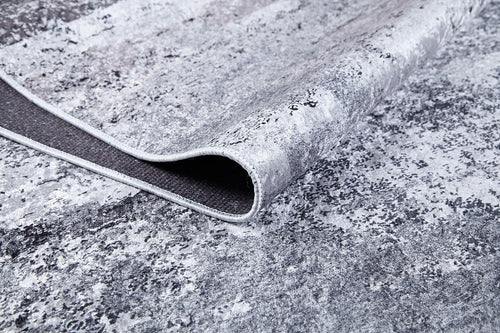 Load image 1 in gallery view. A close-up shows the corner of the Techno Flux - Washable Rug - JR1814 in gray-anthracite, slightly lifted to reveal its dark backing and edge stitching. The marbled, abstract pattern makes it ideal for high-traffic areas.