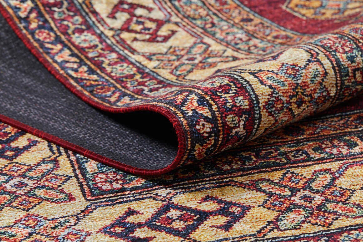 A close-up of the Time-Honored Textures - Washable Rug - JR40 shows its rolled edge, revealing detailed floral and geometric patterns in red, gold, blue, and cream. The visible backing highlights its durability—ideal for high-traffic areas.