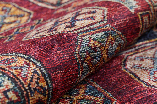 Load image 1 in gallery view. A close-up of the Time-Honored Textures - Washable Rug - JR40 shows a rolled red rug with intricate yellow, white, and blue geometric designs—ideal for high-traffic areas and easy to clean.