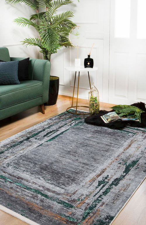 Load image 1 in gallery view. A modern living room with a green sofa, the Traditional and Classic - Washable Rug - JR1543 in gray and green, a round white side table with décor items, a tall potted plant, wooden floors, white walls, and a magazine on the floor.