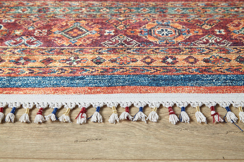 Load image 1 in gallery view. A close-up of the Tropic Thunder - Washable Rug - JR5077 shows its multicolor geometric design in red, blue, and yellow. White, red, and blue tassels line the edge. Perfect for high-traffic areas, it's shown on a light wooden floor.