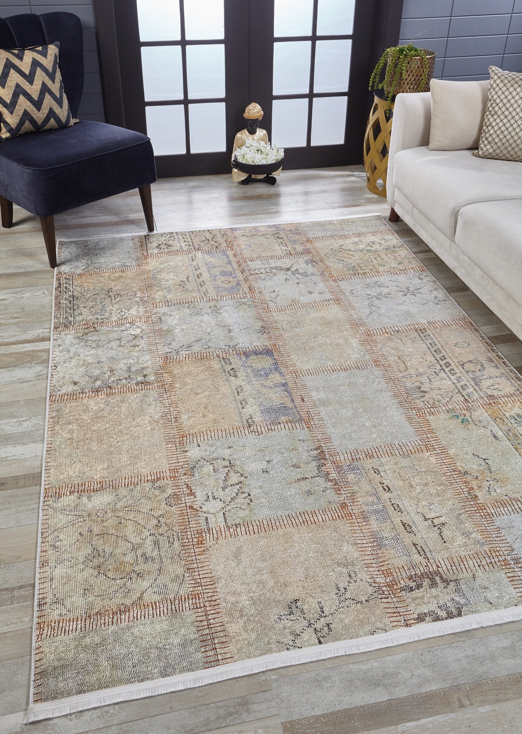 A modern living room features the Urban Utopia - Washable Rug - JR1957 in cream and beige on a light wood floor, paired with a dark blue chair with a chevron pillow, white sofa, potted plant, and double frosted glass doors.
