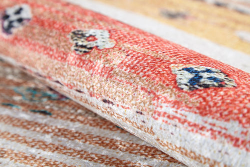 Load image 1 in gallery view. A close-up of the Nomad's Nostalgia - Washable Rug (JR1669) shows its rolled-up multicolor design featuring a red and beige pattern with blue and white floral accents, highlighting the rug's texture and intricate weave.