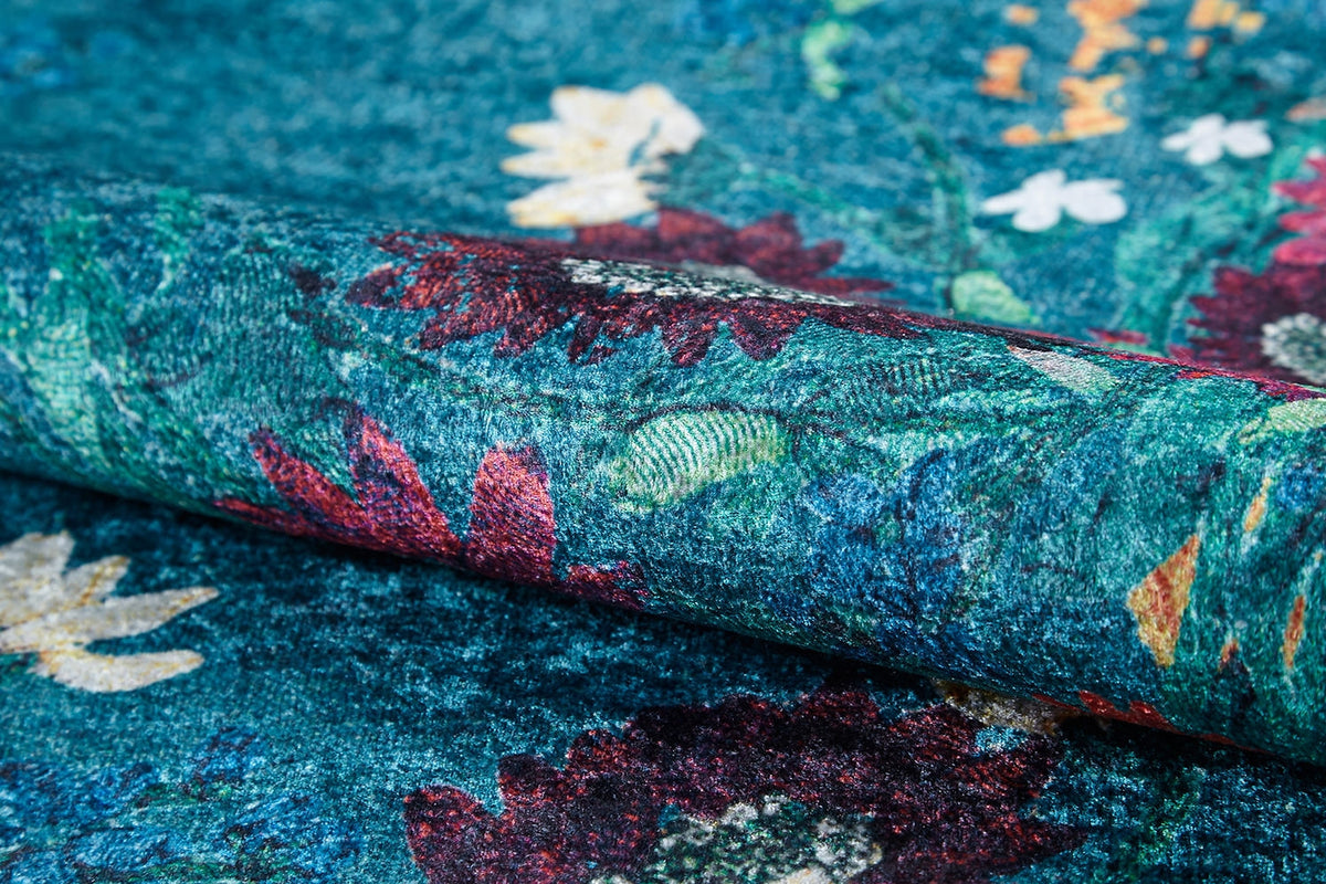 Close-up of the Nature's Tapestry - Washable Rug - JR1674, a teal blue rug rolled up to display its vibrant floral pattern with red, yellow, and white flowers and green leaves. Its soft, slightly raised texture is ideal for high-traffic areas.