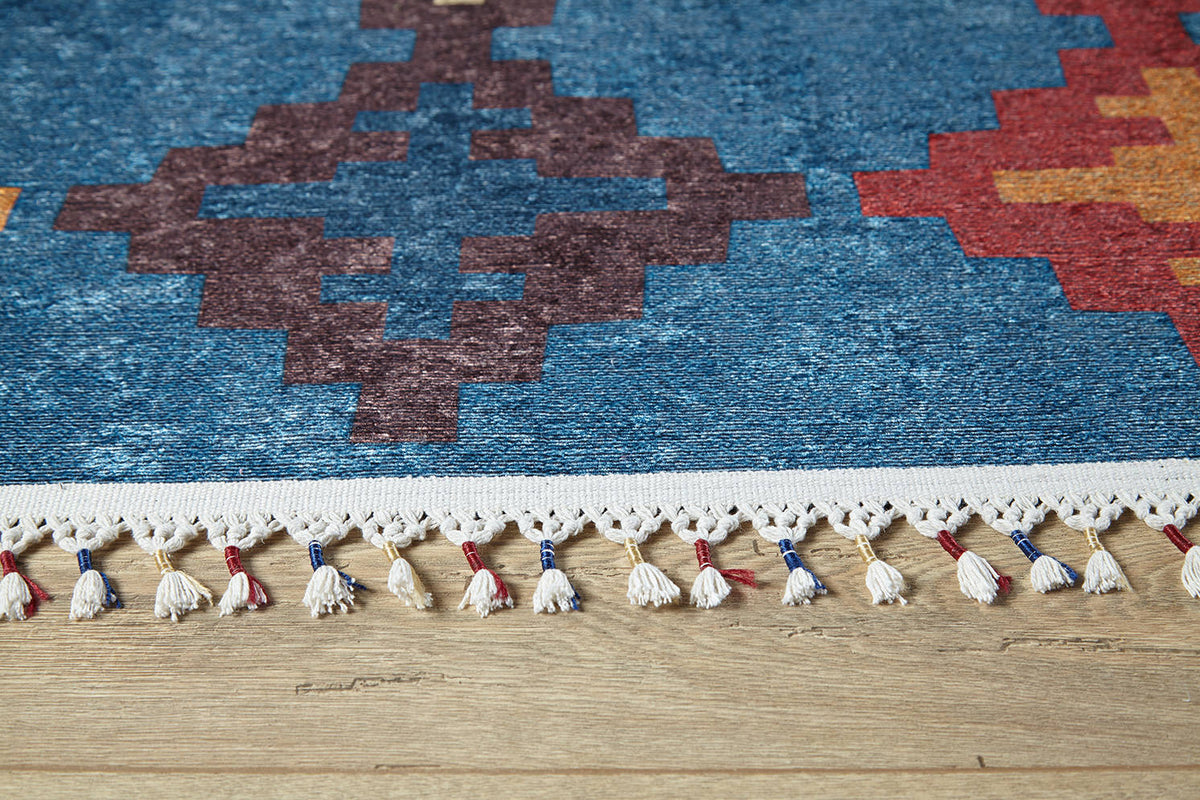 Close-up of the Nomad's Mirage - Washable Rug - JR5032, featuring vibrant geometric patterns in blue, red, and orange. White fringe with red and blue accents adds detail. Ideal for high-traffic areas and displayed on a wooden floor.