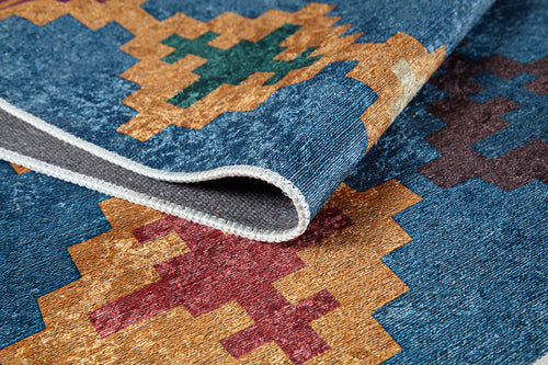 Load image 1 in gallery view. A close-up of the Nomad's Mirage - Washable Rug - JR5032, featuring vibrant geometric patterns in gold, red, green, and blue. The edge and texture are seen as one corner is folded over. Ideal for high-traffic areas.