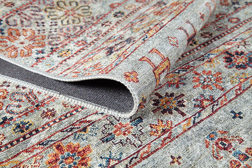 Load image 1 in gallery view. A detailed view of the Nomad’s Nest - Washable Rug - JR5088, showing red, gold, blue, and beige floral and geometric designs with a folded edge to reveal its underside—durable and perfect for high-traffic areas.