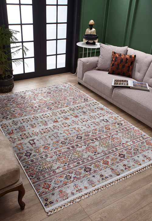 Load image 1 in gallery view. A living room features the Nomad's Nest - Washable Rug - JR5088, perfect for high-traffic areas, paired with a light gray sofa, patterned pillow, small round side table with decor, potted plant, and large black-framed windows filling the space with light.